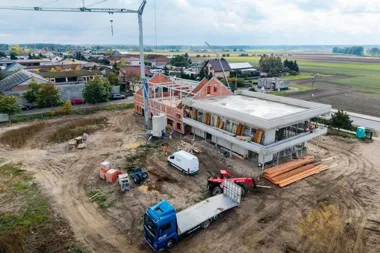Widok z lotu ptaka na budowę nowego obiektu w małej miejscowości, z dźwigiem, ciężarówką i materiałami budowlanymi na placu.